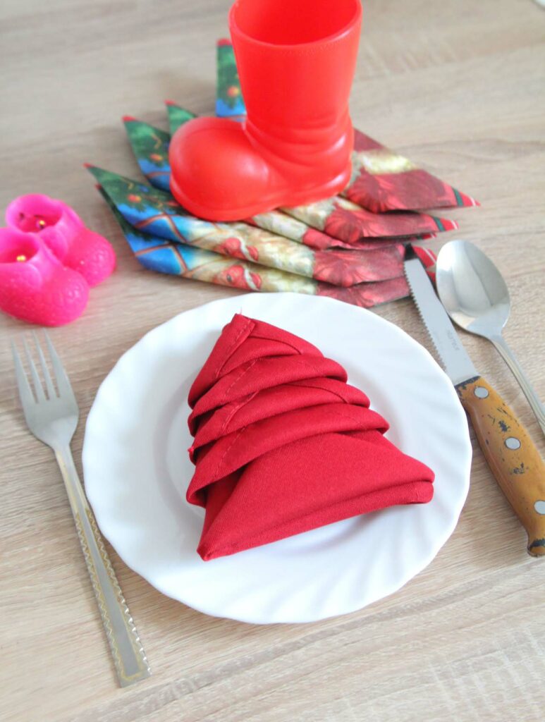 Christmas Tree napkin fold with a red napkin placed on a white plate