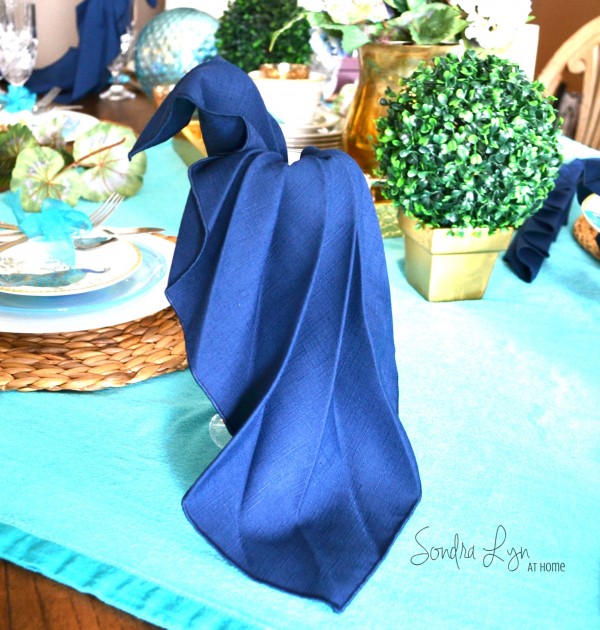 Napkin fold in a peacock shape with a silk blue napkin