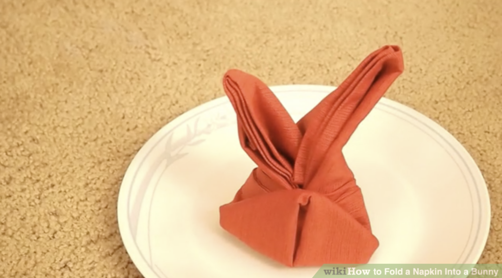 Cute Bunny napkin fold in orange napkin placed on a white plate