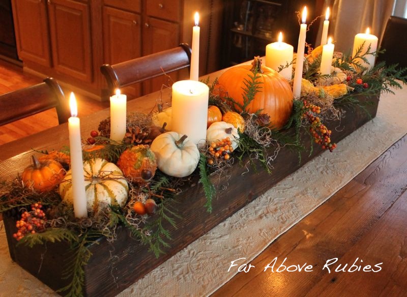 A centerpiece with candles of varying widths and heights surrounded by small pumpkins and fall leaves